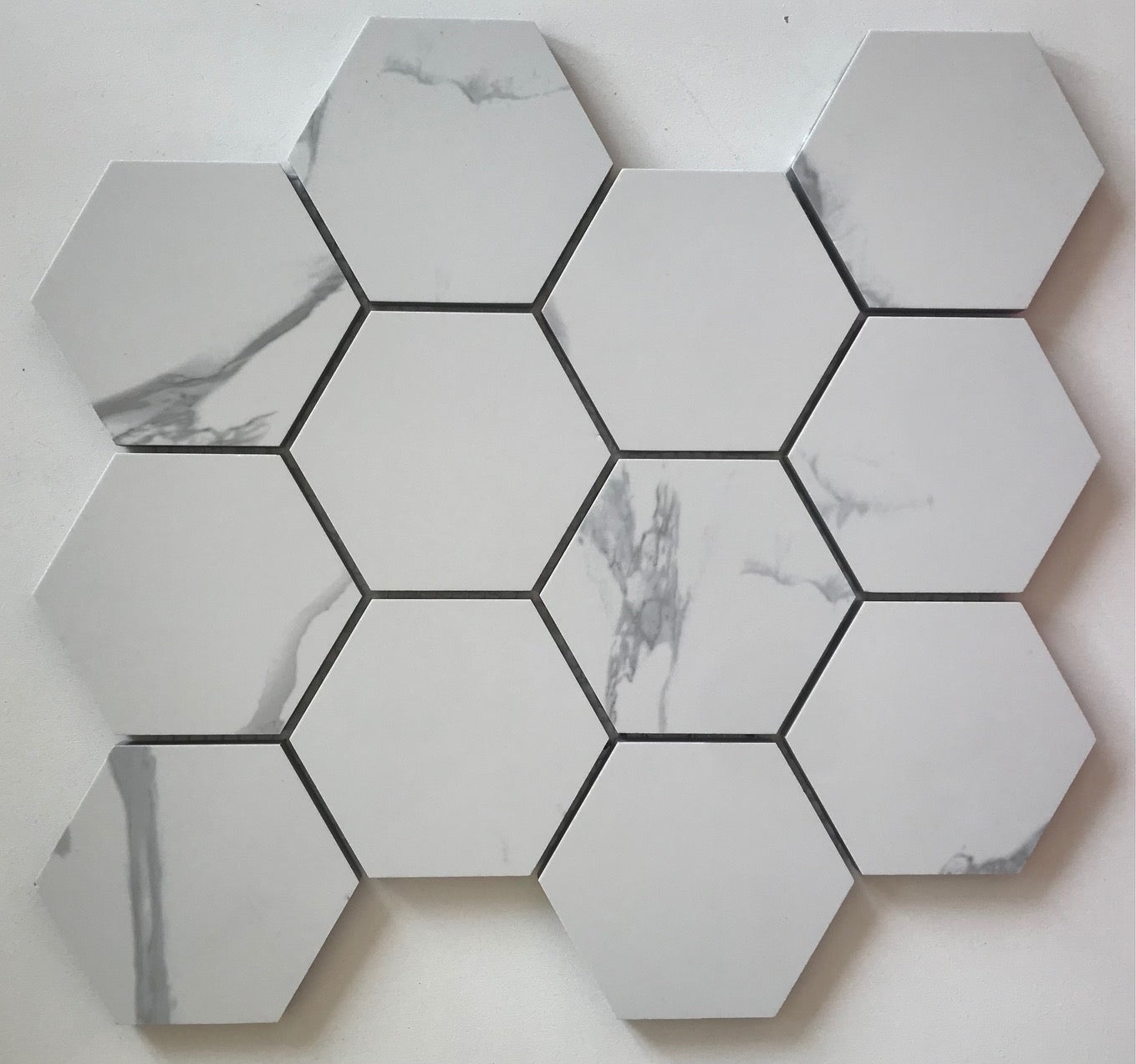 Flat lay of Calacatta Hexagon Porcelain Mosaic sheet with 3-inch marble-look tiles in gray and whit