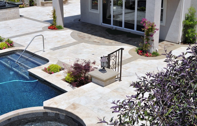 Outdoor tile landscape with travertine pavers, stacked stone walls, and natural pebbles